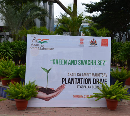 person writing in a notebook beside by an iPad, laptop, printed photos, spectacles, and a cup of coffee on a saucer